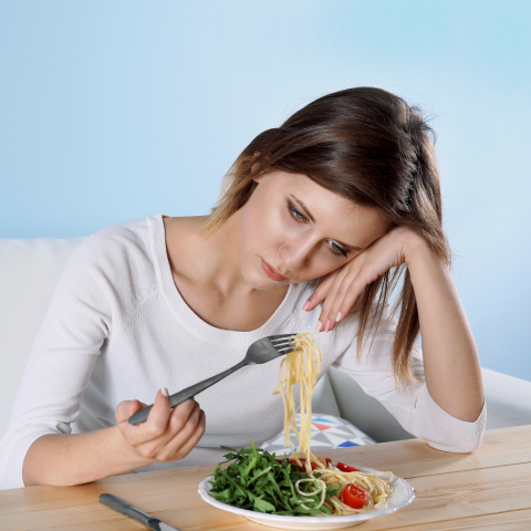 A sad woman stares at a plate of food. 