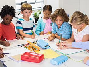 Mixed group of children at table with teacher going over lesson