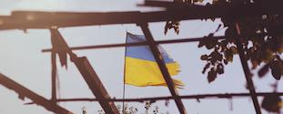 Ukrainian national flag behind damaged house framing